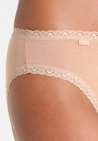 Beige Baumwollslip mit Spitzenbesatz entlang des Bundes. Glatte Textur mit engem Sitz, ausgestattet mit einem kleinen Logostick auf der Seite.