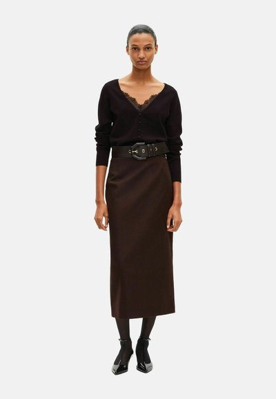 Brun strikket blyantskørt kombineret med en sort cardigan med blonderkant, båret med et bredt sort bælte i taljen og sorte hælede sko.