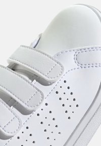 Zapatillas blancas con correas de velcro, material de cuero sintético suave, diseño de punta perforada y suela de goma texturizada.