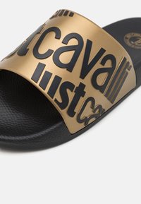 Sandalo a scivolo con una ampia fascia dorata con testo in rilievo nero e una soletta nera texturizzata per aderenza e comfort.
