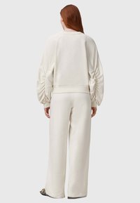 Weißer Sweatshirt mit gerafften Ärmeln und einem verkürzten Design, kombiniert mit passenden weit geschnittenen Hosen. Glattes, weiches Material mit einem lässigen Schnitt.