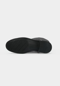 Semelle de botte noire avec des motifs de grip en caoutchouc texturé et un petit talon bloc sur un fond clair uni.