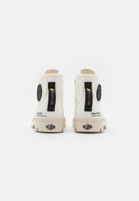 Botines de lona blancos hasta el tobillo con un diseño alto, acentos negros y logo. Incluyen tiradores y suelas de goma texturizadas.