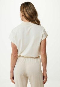 Kortärmad krämfärgad blus med avslappnad passform, mjuk textur och svag lyster, tillsammans med lätta, texturerade byxor med elastisk midja.