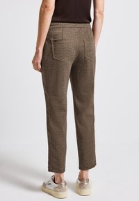 Bruine, gestructureerde broeken met een taps toelopend design. Voorzien van een elastische tailleband en twee achterzakken. G gecombineerd met witte en beige sneakers.