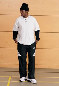 White short-sleeve shirt with black accents, black pants with white stripes, black beanie, and white athletic shoes. Indoor setting.