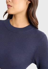 Maglione a coste blu navy con scollatura a girocollo, caratterizzato da maniche corte e un tessuto testurizzato, mostrato dalla spalla in su.