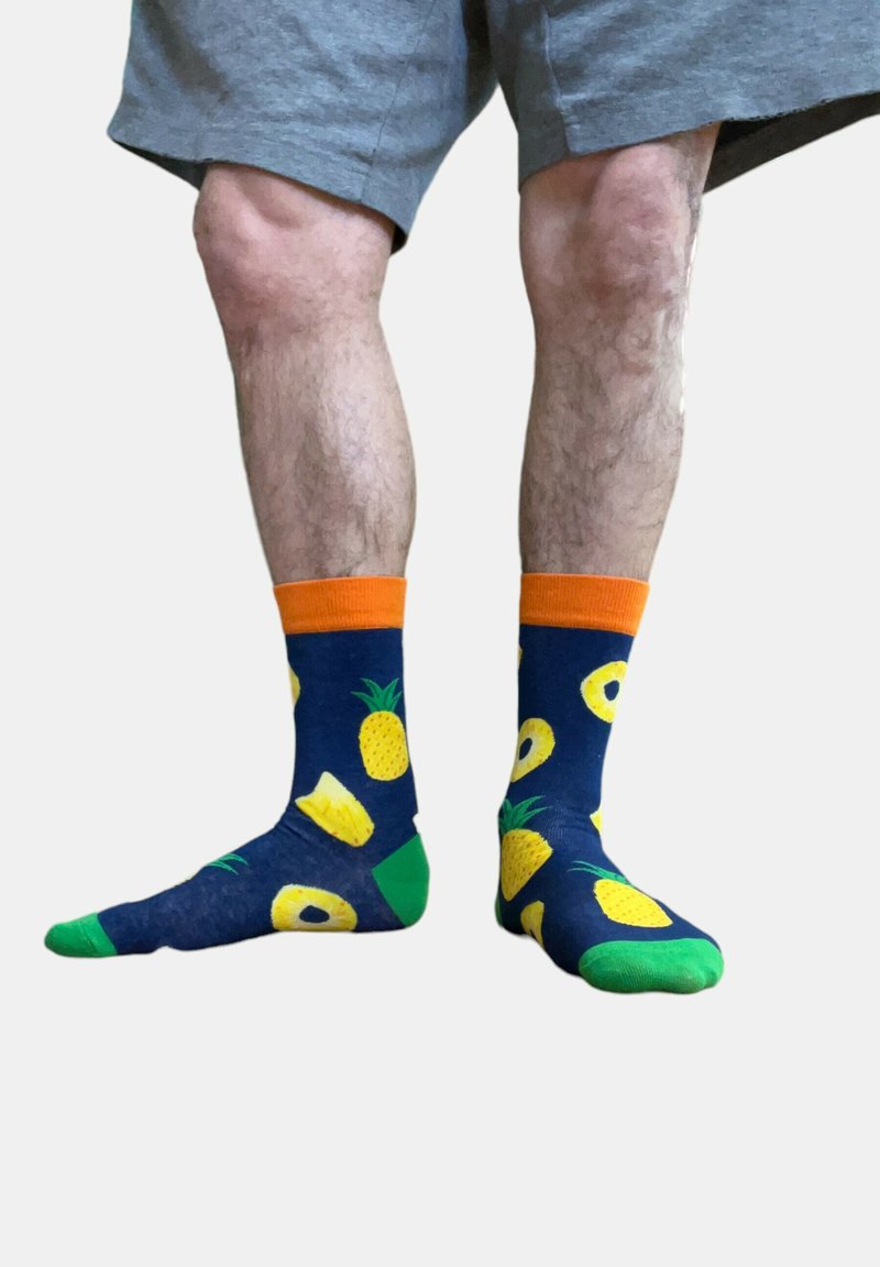 Chaussettes navy avec des motifs d'ananas et de citron, présentant des bords orange et des accents verts. Le matériau semble doux, avec une texture lisse.