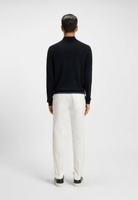 Maglietta nera a maniche lunghe con colletto, abbinata a pantaloni bianchi. La maglietta presenta un design pulito; l'outfit ha un semplice contrasto di colori.