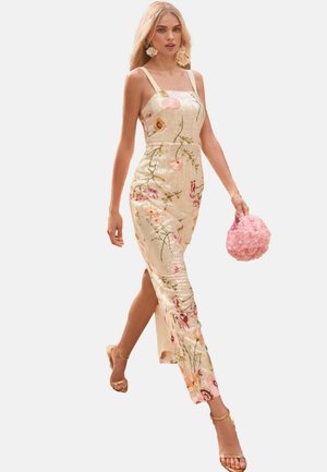 Hame dengan lengan tanpa, berkilau emas dengan bordiran bunga, belahan tinggi, dan siluet yang pas. Dipasangkan dengan tas tangan berbentuk bunga berwarna pink dan sandal emas.