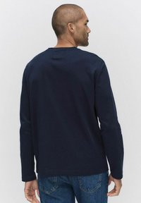 Laivastonsininen pitkähihainen t-paita, joka on valmistettu puuvillasta. Siinä on pyöreä kaula-aukko, rento malli ja ommellut yksityiskohdat helmassa ja hihoissa.