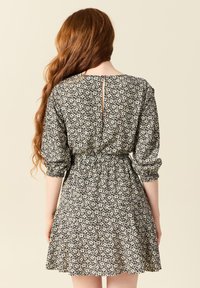 Svart blommig klänning med figurnära midja, 3/4 ärmar och en nyckelhål på baksidan. Har en utsvängd kjol och delikata vita blommönster.
