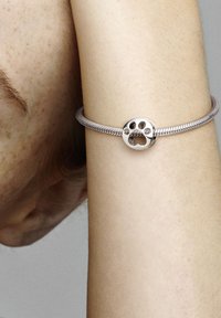 Bracciale in argento con un ciondolo rotondo dal design con impronta di zampa, caratterizzato da una texture intrecciata e una finitura lucida.