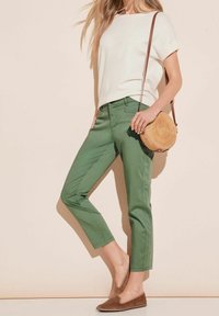 Pantalons verts coupés, ajustés, associés à un haut blanc à manches courtes. Accessoirisés avec un sac rond en paille et des chaussures brunes à enfiler.