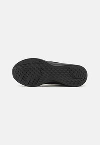 Semelle de chaussure noire avec motif de grip texturé et design courbé, vue de dessous sur un fond clair uni.