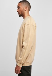 Sudadera beige con cuello redondo, hombros caídos y puños acanalados. Fabricada en un suave tejido texturizado, diseñada para un ajuste relajado.