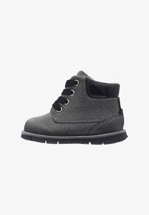 Grauer Kleinkinderstiefel mit schwarzen Schnürsenkeln, glänzendem schwarzen Schaftabschluss und dicker schwarzer Sohle, von der Seite auf weißem Hintergrund gezeigt.