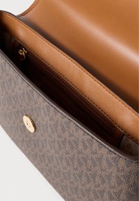 Καφέ τσάντα με σχέδια, διαθέτει χρυσό κούμπωμα και λείο ταμπά εσωτερικό, που περιλαμβάνει φερμουάρ και κομψή επένδυση.