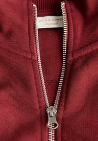 Burgunderfärgad zip-up sweatshirt med silverdragkedja, ribbat krage och mjuk textur. Etiketten visar "Jack & Jones Originals" inuti.