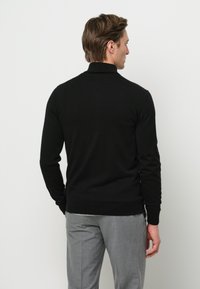 Pullover nero attillato con maniche a costine. Indossato con pantaloni grigi, presenta un design pulito e minimalista con una texture morbida.
