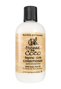 Witte plastic fles met een zwarte geribbelde dop. Bevat beige tekst op een lichte achtergrond. Gelabeld als "Bumble and Bumble creme de Coco CONDITIONER."
