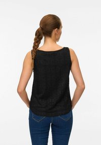 Czarny bezrękawnik z fakturowanym okrągłym wzorem; okrągły dekolt; noszony z niebieskimi dżinsami, co podkreśla swobodny styl.