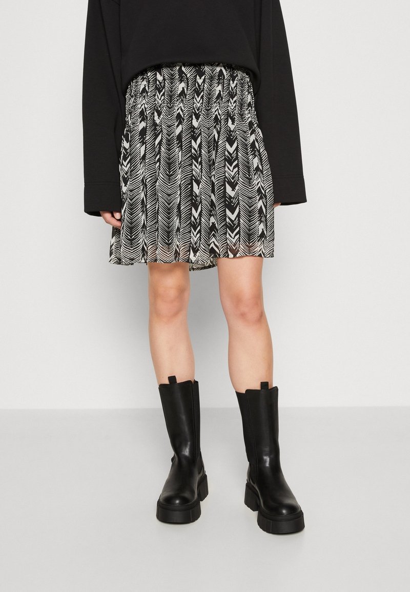 Jupe à motif noir et blanc avec une taille smockée, associée à des bottes en cuir noir hauteur genou avec une semelle épaisse.