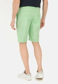 Lichtgroene shorts van lichtgewicht stof, met zijzakken en een nette afwerking. Draagt een casual stijl met witte sneakers.