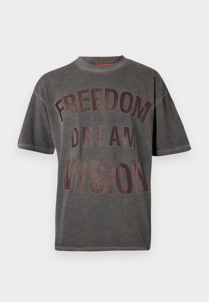 Harmaa ylisuurikokoinen t-paita, jossa on painettu teksti "FREEDOM DREAM VISION", yhdistetty tummiin farkkuihin ja mustiin kenkiin. Mukana musta olkalaukku.