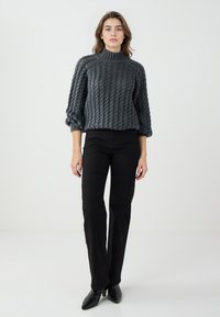 Maglione a collo alto grigio scuro lavorato a maglia con motivo testurizzato, abbinato a pantaloni neri a gamba dritta a vita alta e décolleté neri a punta.