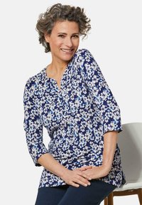 Blumige Tunika in Marineblau mit weißen und hellblauen Blumen, mit V-Ausschnitt, Dreiviertelärmeln und weichem, leichtem Stoff.