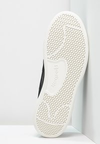 Sneakers noires avec une tige en tissu texturé, dotées d'une semelle en caoutchouc blanc avec un motif de semelle en nid d'abeille et une marque en relief.