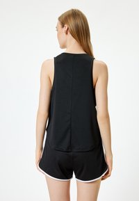 Top negro sin mangas con escote redondo y corte holgado, combinado con pantalones cortos negros con ribetes blancos en los bordes.