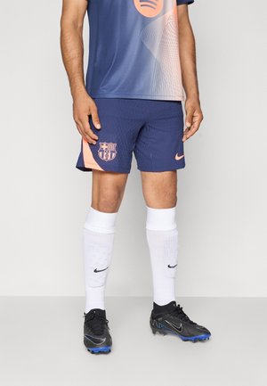 FC Barcelona-trøje i marineblå og gradient ferskenfarver, parret med marineblå shorts med klublogo. Sorte støvler og hvide sokker.