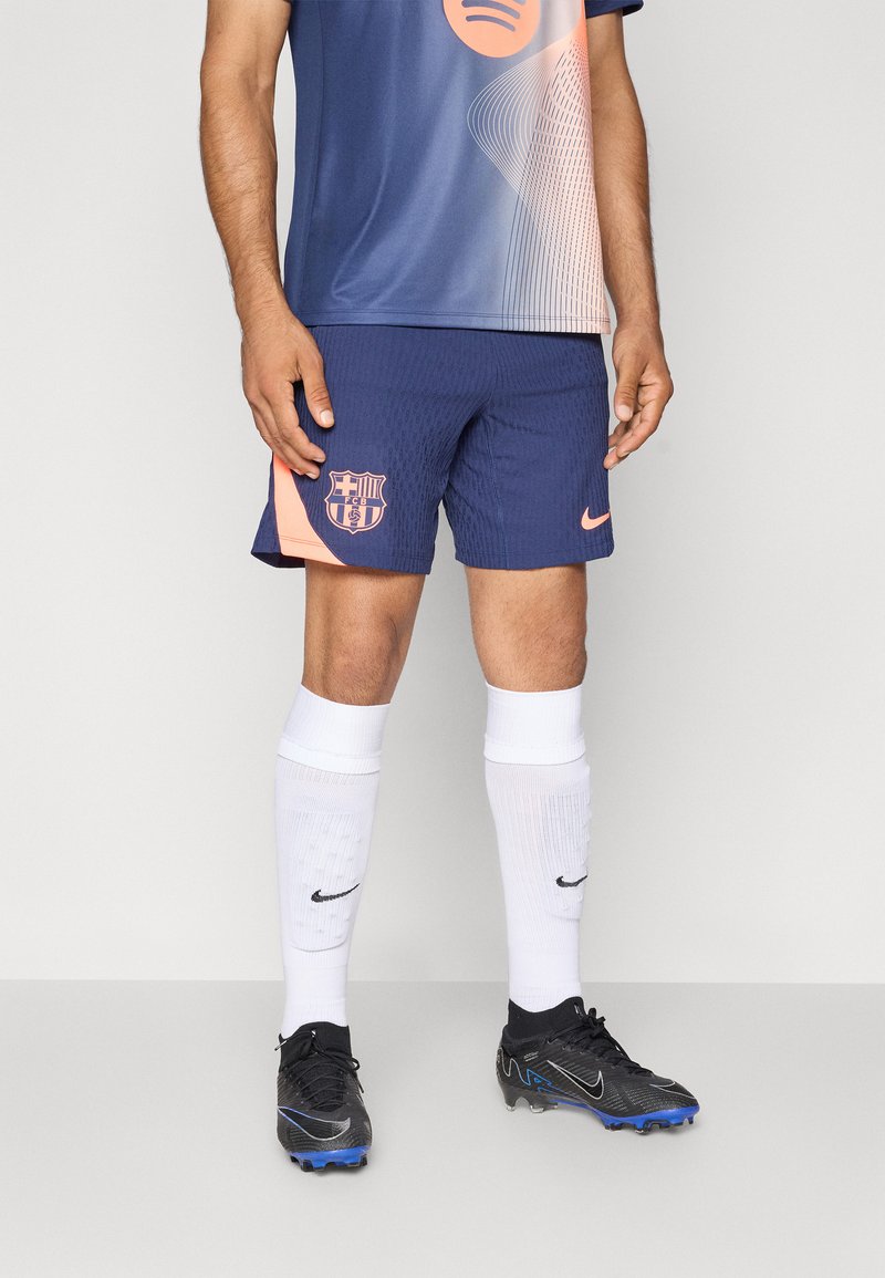 FC Barcelona-drakt i marineblå og gradient ferskenfarger, parret med marineblå shorts med klubbens logo. svarte fotballsko og hvite sokker.