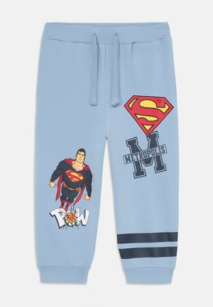 Šviesiai mėlynos medvilninės sportinės kelnės su "Superman" grafika, įskaitant raudoną logotipą ir juodą tekstą. Apatinėse dalyse yra tamsiai mėlyni dryžiai.