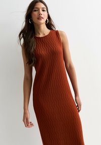 Robe sans manches, longue jusqu'au sol, de couleur rouille avec un motif en zigzag texturé. Présente un col rond et une silhouette cintrée.
