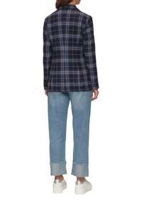 Marineblauwe geruite blazer met blauwe en witte accenten; gecombineerd met lichtblauwe opgerolde jeans en zilveren sneakers, wat een ontspannen silhouet laat zien.