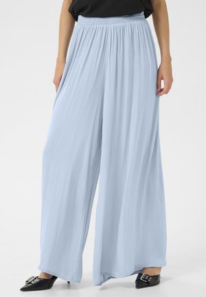 Hellblaue, weit geschnittene Hose mit elastischem Bund, kombiniert mit schwarzen spitzen High Heels und einem schwarzen Oberteil, dargestellt von der Taille bis zu den Füßen.