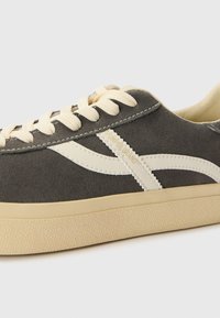 Sneakers en suede gris avec des lacets crèmes et des accents latéraux. Présente une semelle en caoutchouc texturé et le logo "POMPEII BRAND" sur le côté.