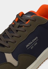 Baskets bleu foncé et olive avec lacets marron, doublure intérieure orange, et marquage "Jack & Jones EST. 1990" sur le côté.