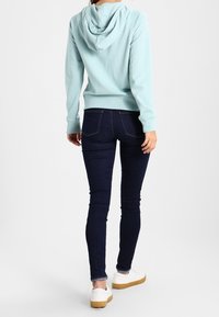 Sweat à capuche bleu clair avec une capuche arrière, associé à un jean skinny bleu foncé et des chaussures blanches à semelle brun clair. Design simple, style décontracté.