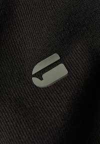 Gros plan sur un tissu noir à texture côtelée, avec un logo en relief de couleur vert clair sur la surface.