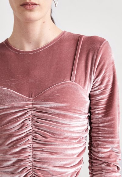 Rosa Samt Langarmshirt mit Rundhalsausschnitt, gerafftem Vorderteil und gerafften Ärmel für Textur und visuelles Interesse.