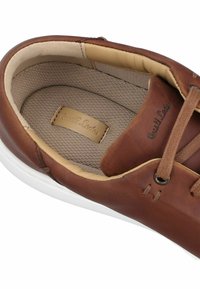 Brauner Lederschnürschuh mit gepolstertem, beigeem Innenfutter und weißer Gummisohle, mit einem eingenähten Markenlabel innen.