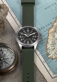 Timex Expedition kell, millel on päikeseenergial toimiv must kellakujundus valgete numbritega, roheline kummirihm ja roostevabast terasest korpus.