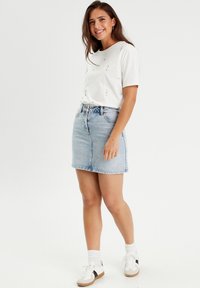 White short-sleeve t-shirt with rhinestone accents, paired with a light blue denim skirt. Model wears white sneakers with black accents.