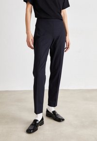 Navy tailored trousers with a slim fit, featuring a smooth texture, front creases, and a mid-rise waist. Paired with black loafers and white socks.