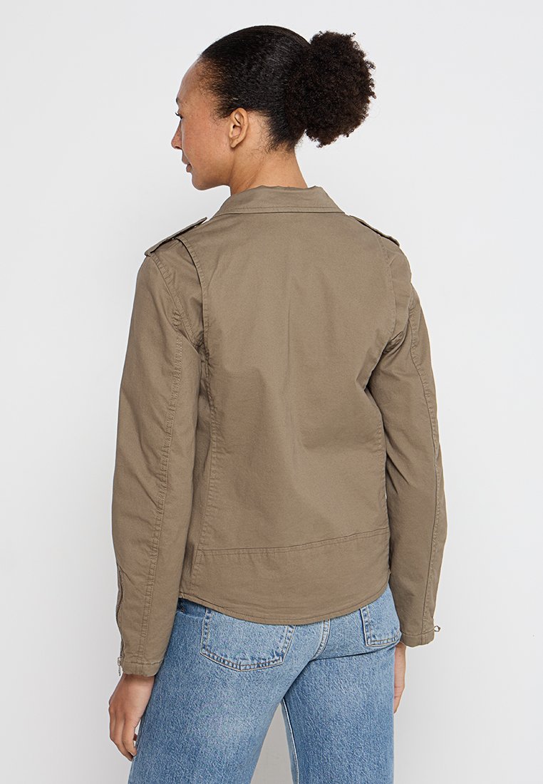 Veste vert olive au design structuré, avec épaulettes et manches longues. Le tissu semble léger, adapté pour le superposition.