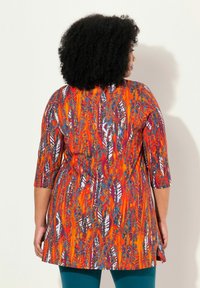 Een meerkleurige tuniek heeft driekwart mouwen, een getailleerde taille en een uitlopende zoom. De stof heeft een levendig abstract patroon met oranje, blauw en paars.